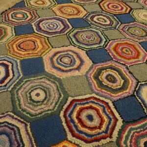 Textured rug with multicolored concentric hexagons alternating with solid blue and gray squares.