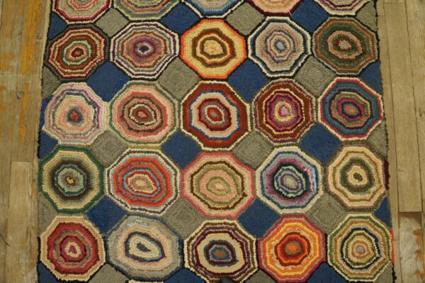 Textured rug with colorful hooked octagons separated by blue and grey square shapes resting on wooden floors.