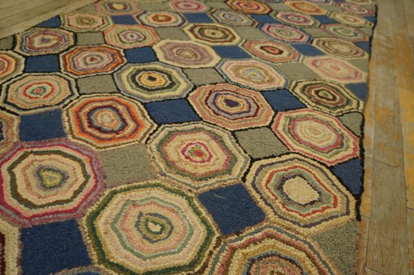 A multicolor hooked rug featuring geometric hexagons with concentric rings and contrasting blue and gray squares on wood flooring.