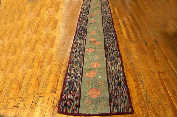 A sage floral runner with multicolored strip borders lies centered on glossy amber wood flooring.