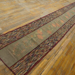 A long green and pink floral runner rug with striped multicolored borders rests on worn hardwood floors.