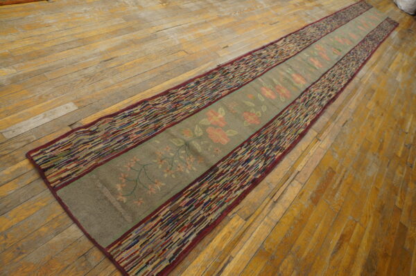 A long green and pink floral runner rug with striped multicolored borders rests on worn hardwood floors.