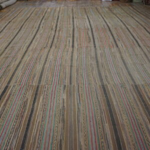Wide, neutral flatweave rug with multicolored and solid brown vertical stripes covering a wood floor.