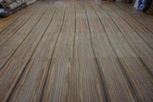 Wide, neutral flatweave rug with multicolored and solid brown vertical stripes covering a wood floor.
