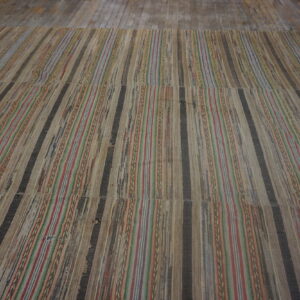 Striped flatweave rug showing woven tan, dark, red, and blue strips on rustic wooden floorboards.