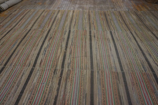 Striped flatweave rug showing woven tan, dark, red, and blue strips on rustic wooden floorboards.