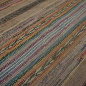 Close-up of a low-pile striped rug with woven multicolored strips in brown, blue, purple, and gray.
