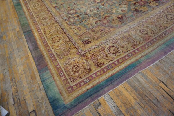 Traditional floral rug in teal, gold, and purple borders rests on worn plank hardwood flooring.