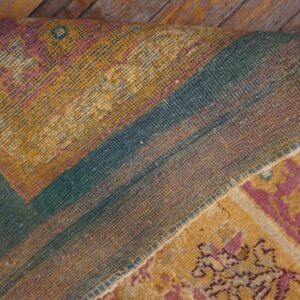 Yellow, pink, and teal patterned rug is folded, revealing its woven backing on distressed wooden planks.