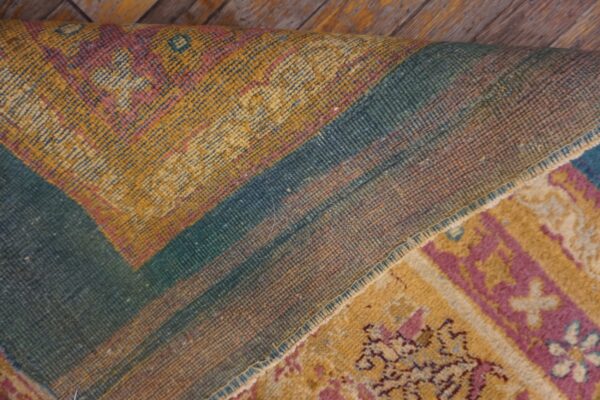 Yellow, pink, and teal patterned rug is folded, revealing its woven backing on distressed wooden planks.