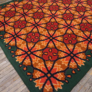 High-pile rug with a repeating orange, red, and brown lattice pattern and a solid green border on wood floors.
