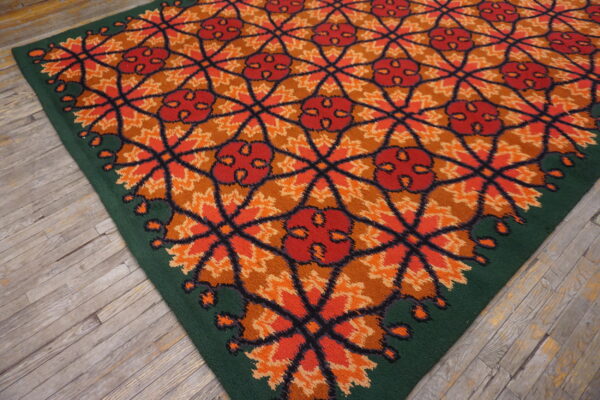 High-pile rug with a repeating orange, red, and brown lattice pattern and a solid green border on wood floors.