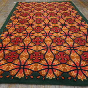 Vibrant orange and red geometric runner rug with a dark green border rests on distressed wooden flooring.