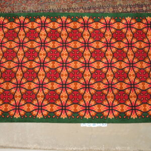 Red, orange, and green high-pile rug featuring a geometric lattice pattern on light concrete flooring.