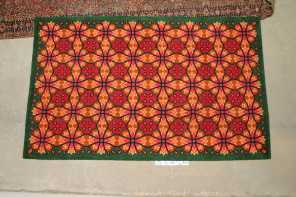 Red, orange, and green high-pile rug featuring a geometric lattice pattern on light concrete flooring.