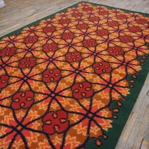 High-pile red and orange rug featuring a geometric floral lattice, bordered by dark green on wood flooring.