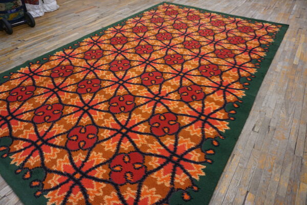 High-pile red and orange rug featuring a geometric floral lattice, bordered by dark green on wood flooring.
