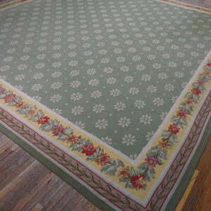 Sage green rug with white daisy pattern and detailed floral borders rests on rustic hardwood floors.