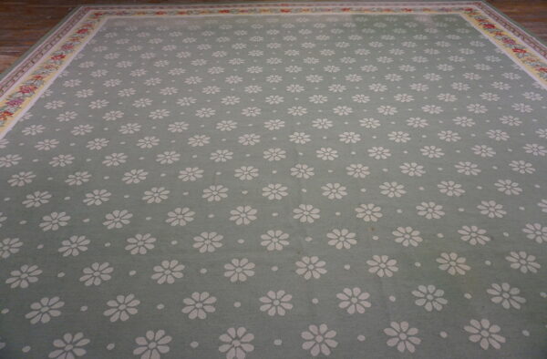 Light sage rug with repeating white daisies and a detailed floral border on wood flooring.