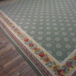 Green rug with white floral patterns and a wide yellow border featuring colorful flower garlands on distressed hardwood flooring.