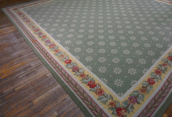 Green rug with white floral patterns and a wide yellow border featuring colorful flower garlands on distressed hardwood flooring.