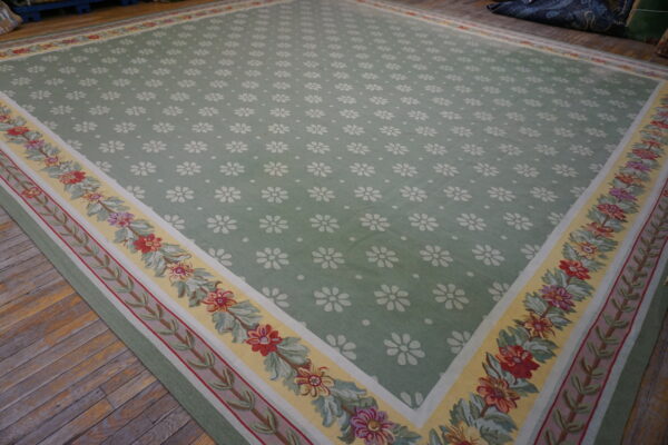 Sage green low pile rug with white repeating flowers and a colorful floral garland border on wood floors.