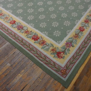 Light green rug with white daisy motifs and a colorful floral border sits on rustic wood planks.