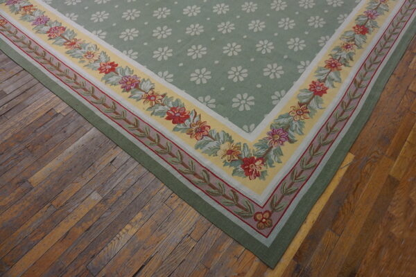 Light green rug with white daisy motifs and a colorful floral border sits on rustic wood planks.