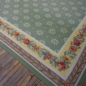 Low-pile green rug with white daisy motifs and a colorful floral border on rustic hardwood flooring.
