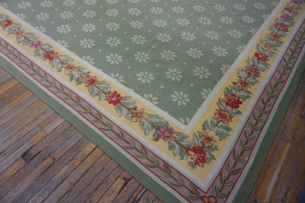 Low-pile green rug with white daisy motifs and a colorful floral border on rustic hardwood flooring.