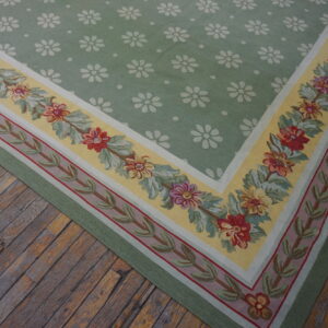 Low-pile rug with a green repeating floral field and elaborate yellow and red flowered border on rustic wood.