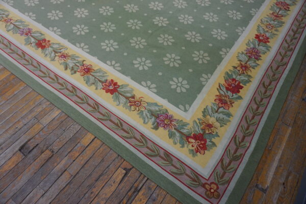 Low-pile rug with a green repeating floral field and elaborate yellow and red flowered border on rustic wood.
