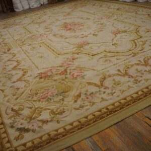 Cream and gold traditional rug with pink roses covers a distressed wooden floor.