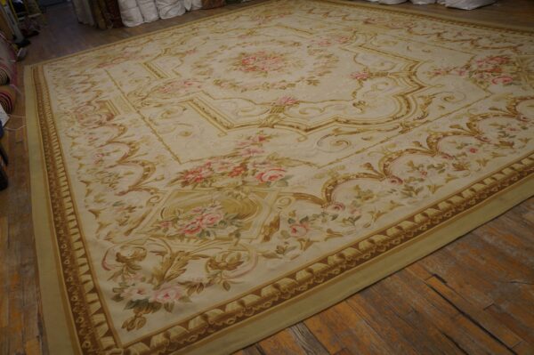 Cream and gold traditional rug with pink roses covers a distressed wooden floor.