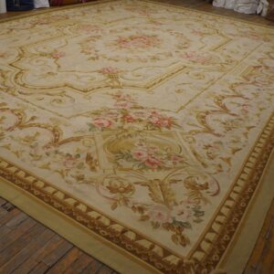 Oversized rug with a cream ground, ornate gold scrollwork, and painted pink floral details on wood floor.