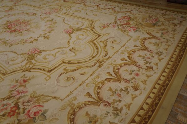 A large low-pile rug featuring a cream background with gold scrollwork and pink floral bouquets on wood flooring.