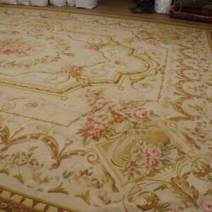 Cream rug featuring neoclassical gold scrollwork and garlands of pink and green roses on distressed wood flooring.