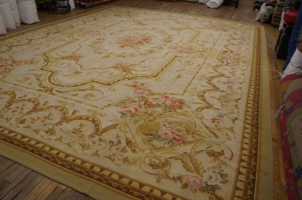 Ornate ivory rug with scrolled gold borders and pink floral accents lies on a wooden floor.