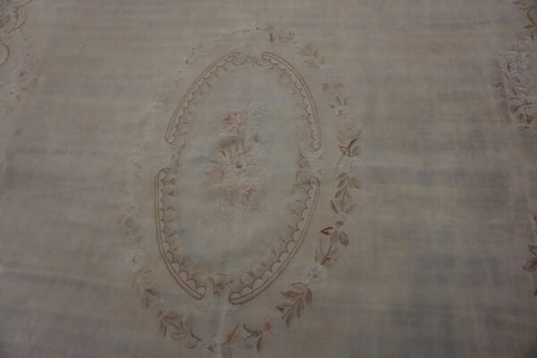 A pale beige rug with a central oval medallion featuring pink roses and surrounding floral borders.