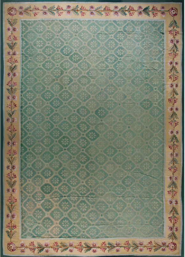 Muted teal rug with a lattice pattern and wide beige border featuring mauve and green floral motifs.