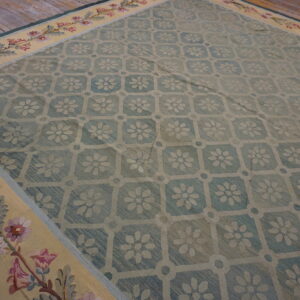 A blue floral lattice rug with a wide yellow border of pink and purple flowers on rustic wood floors.