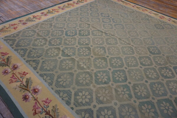 A blue floral lattice rug with a wide yellow border of pink and purple flowers on rustic wood floors.