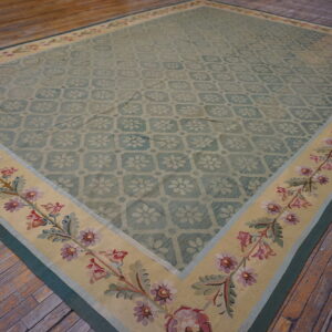 A pale green low-pile rug with a floral pattern and beige botanical border rests on rustic wood planks.