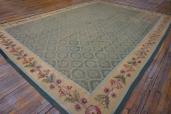 A pale green low-pile rug with a floral pattern and beige botanical border rests on rustic wood planks.