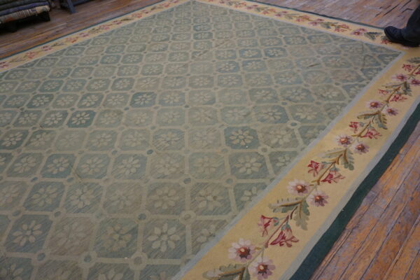 Teal and beige floral medallion rug with a wide yellow border and pink flowers, lying on wood floors.