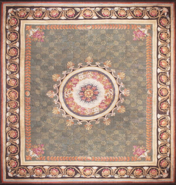 A large green rug with an ornate floral medallion center and multi-layered borders in pink, cream, and brown.
