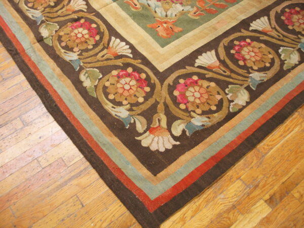 Flat-woven rug corner featuring dark brown, green, red, and gold scrolling floral patterns on wood flooring.