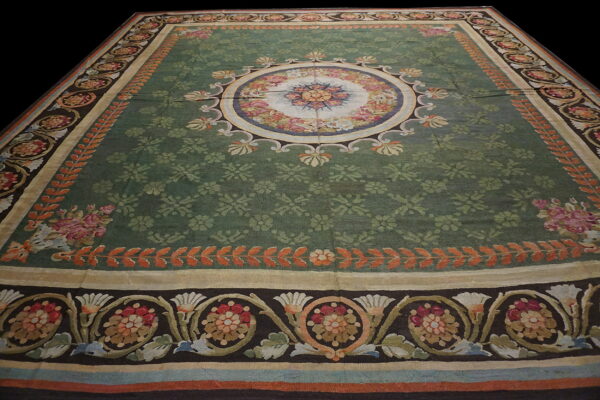 Ornate low-pile rug with a sage green field, a central floral medallion, and dark multi-color borders.