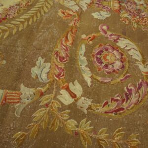 Brown distressed rug with large floral motifs and scrollwork in faded pink, gold, and cream colors.