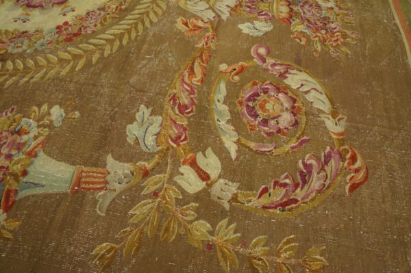 Brown distressed rug with large floral motifs and scrollwork in faded pink, gold, and cream colors.